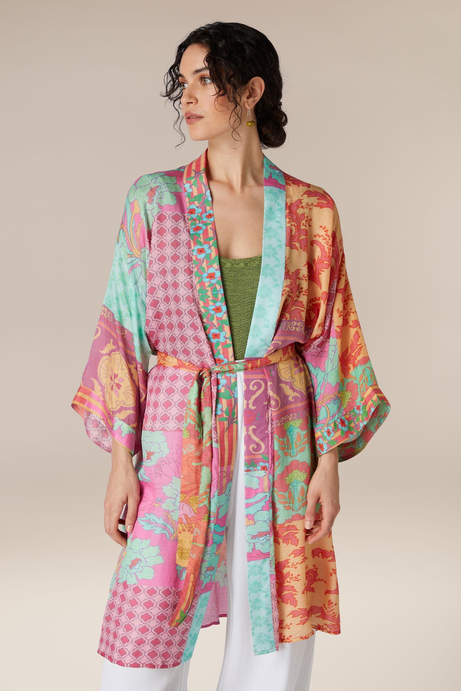 Woman modeling a Geometric Floral Silk Kimono with geometric floral patterns, paired with white trousers and a green top.