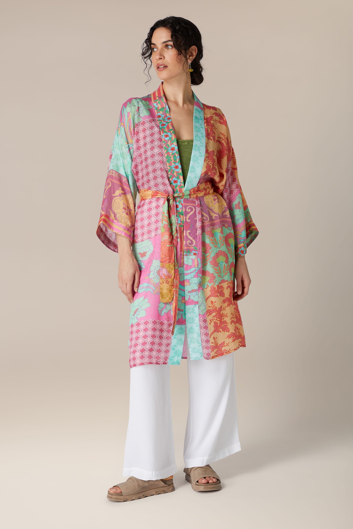 Woman posing in a luxurious Geometric Floral Silk Kimono jacket with geometric floral patterns, paired with white trousers and sandals.