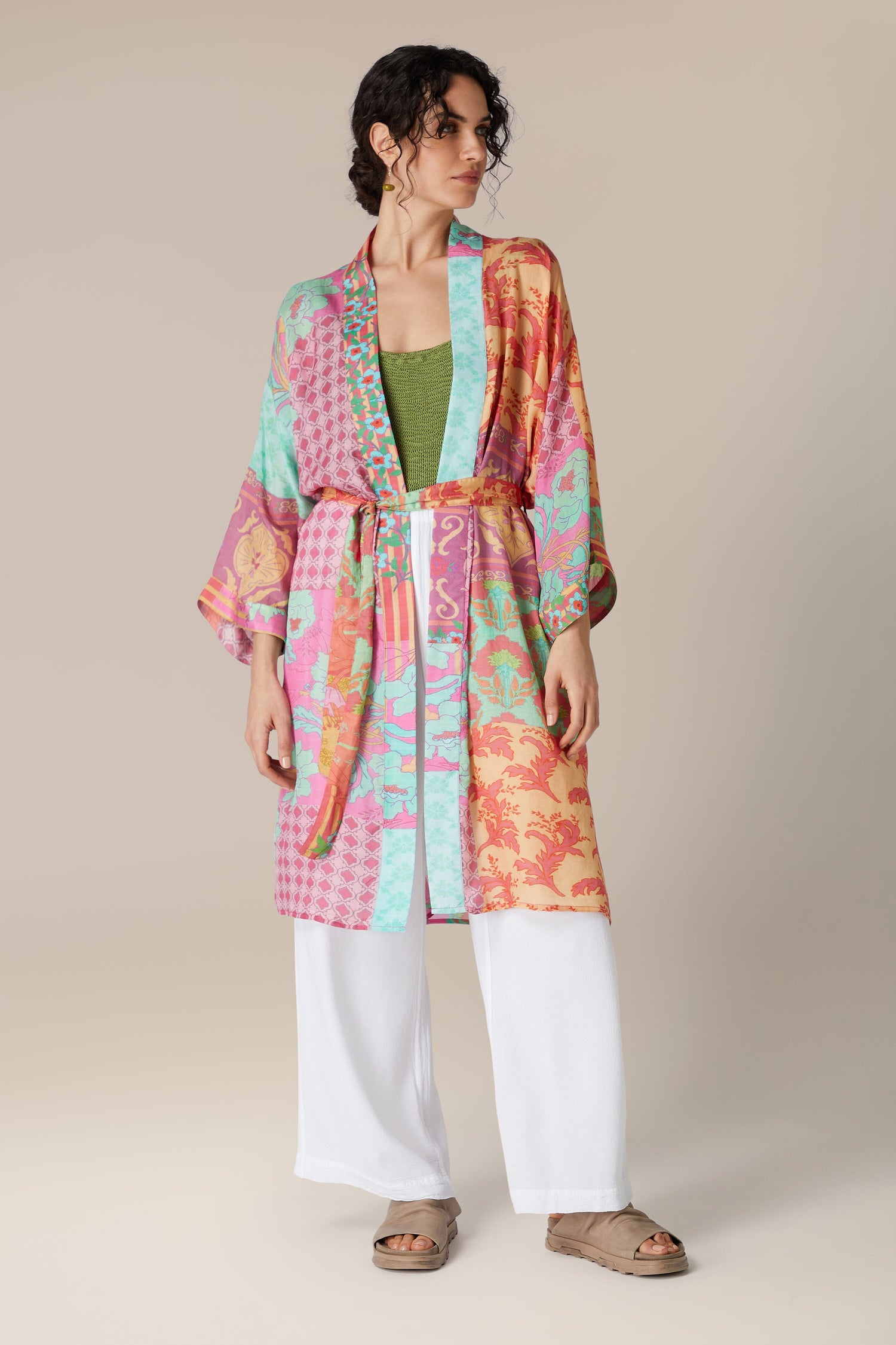 A woman wearing a vibrant, multicolor Geometric Floral Silk Kimono over a green top and white trousers, posing against a neutral background.