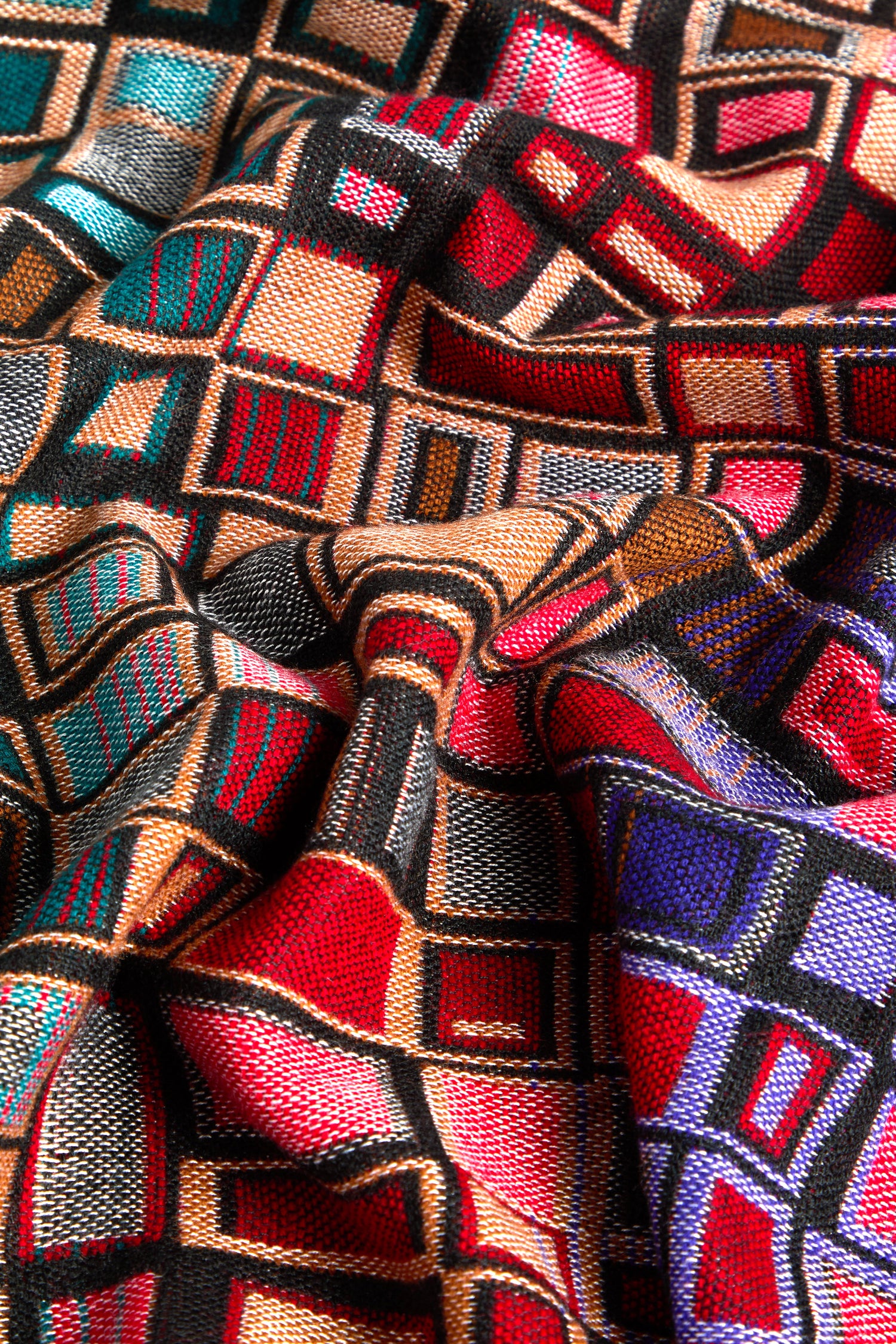 Close-up of the intricately woven Tesserae Scarf displaying a colorful geometric pattern with intersecting squares and rectangles in shades of red, blue, green, and yellow, giving this vibrant accessory a touch of contemporary flair.