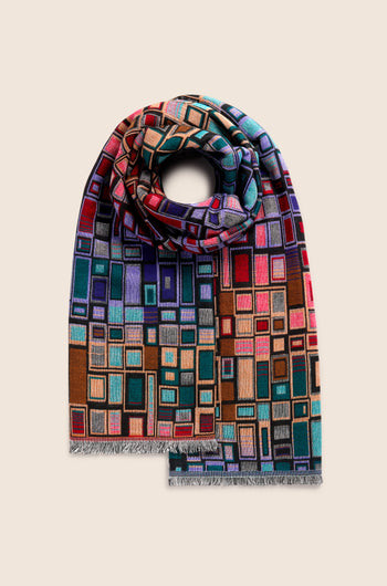 The Tesserae Scarf, rolled up and displayed on a plain beige background, features a vibrant abstract geometric pattern with squares and rectangles that add a touch of contemporary flair.