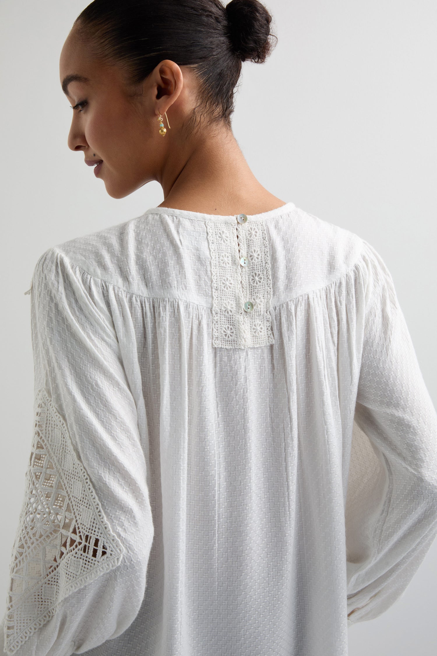 The person wears a white Floral Lace Trim Top, featuring lace-detailed sleeves. From the back, the blouse's charm is highlighted by elegantly descending button accents.