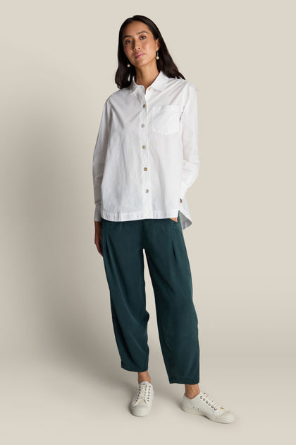 A person wearing a Curved Hem Shirt, teal pants, and white sneakers stands against a plain background.