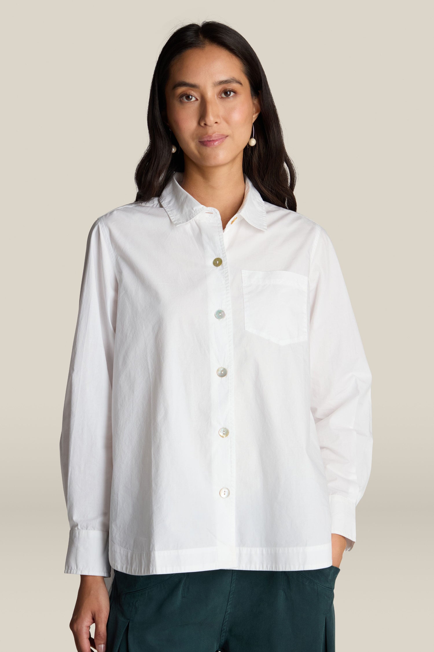 A person with long dark hair is wearing the Curved Hem Shirt, a white premium cotton shirt, along with dark pants, standing against a light background.