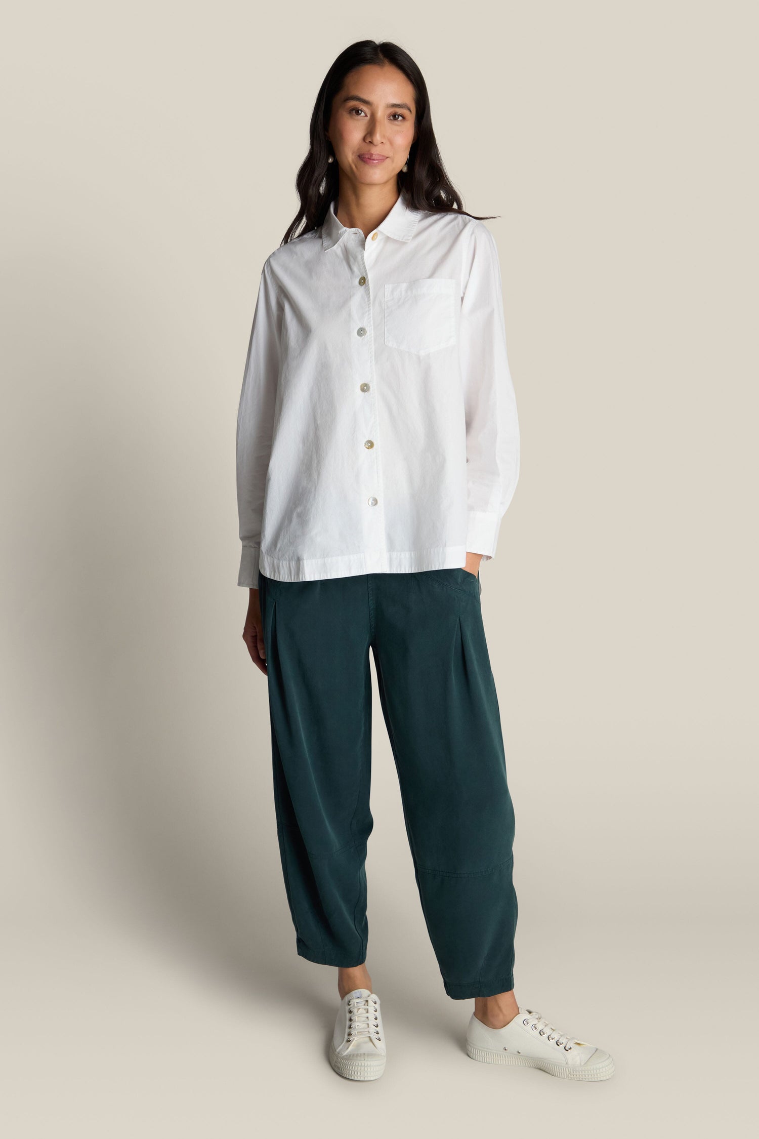 A person standing against a plain background, wearing the Curved Hem Shirt made of premium cotton, dark green pants, and white shoes.