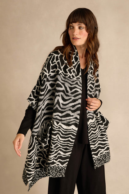 A woman wears the Abstract Jacquard Merino Wool Jacket, featuring a bold monochrome jacquard pattern in black and white, styled over black clothing and set against a neutral background.