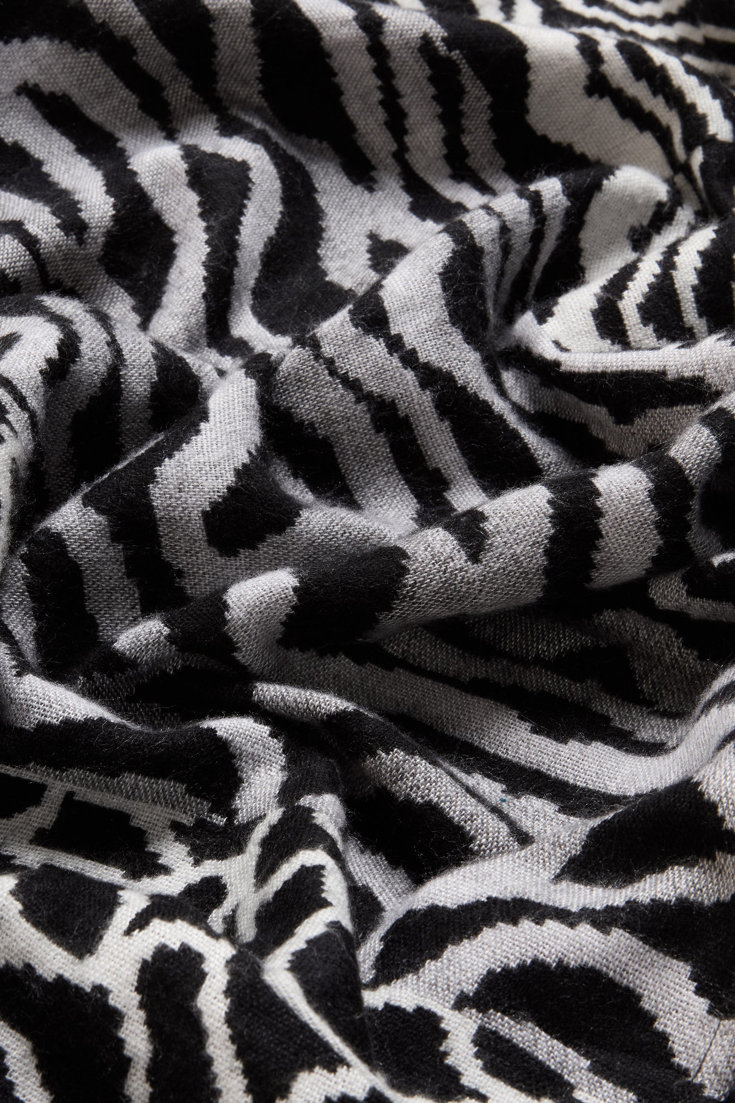 Close-up of the Abstract Jacquard Merino Wool Jacket, highlighting its bold black and white geometric pattern and visible folds and texture, which showcase the striking monochrome design created through intricate jacquard construction.