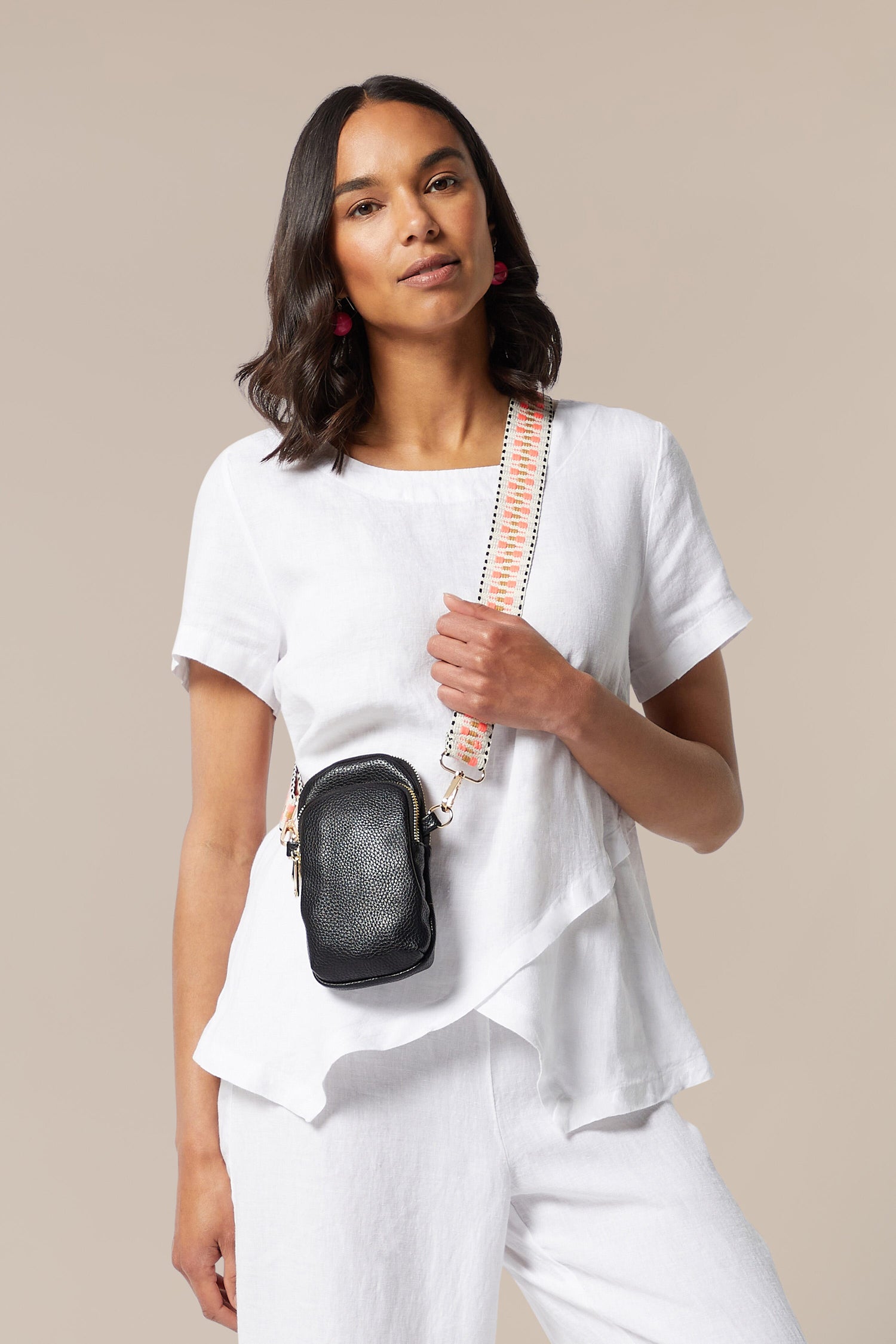 A woman wearing white pants and a black fanny pack showcasing the stylish Kris-Ana Mini Crossbody Bag.