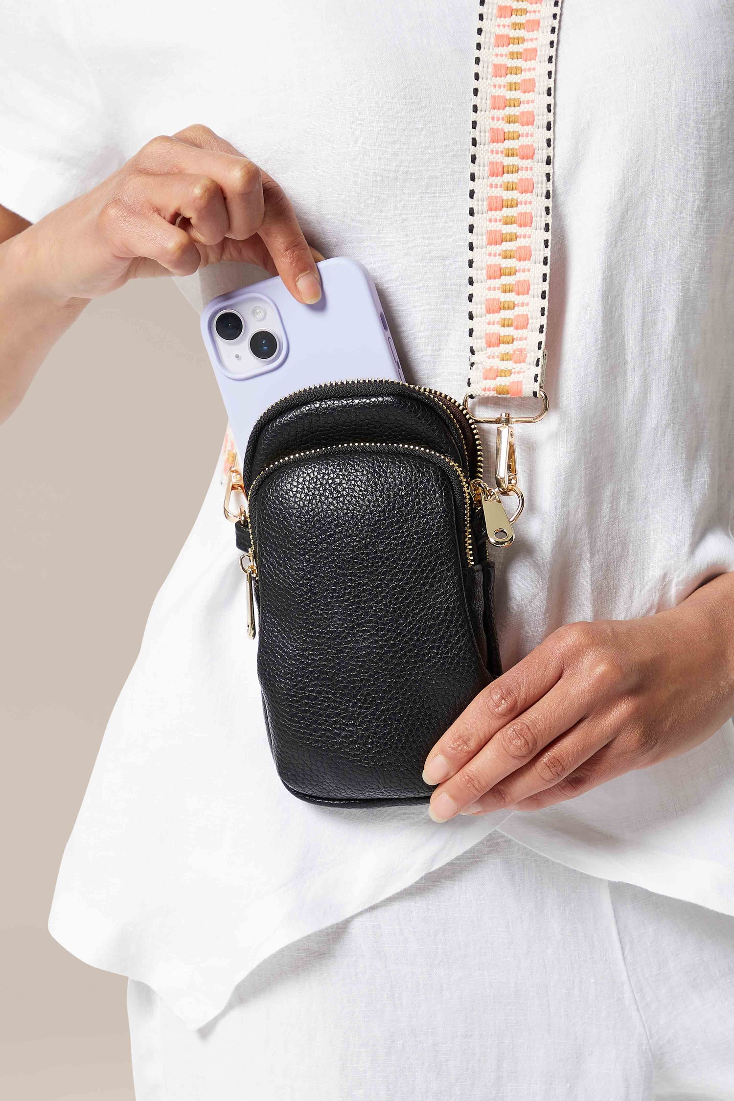 A woman holding an iPhone with a Mini Crossbody Bag.