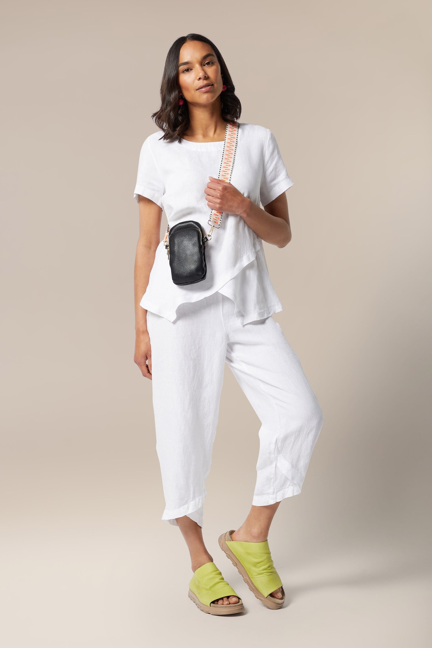 A woman, stylishly dressed in white pants and a white t-shirt, carrying a Mini Crossbody Bag.