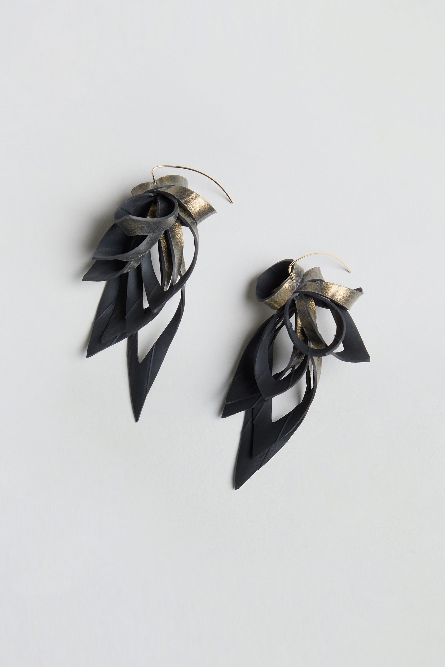 Gold Flipped Leaves Earrings, crafted from reclaimed bicycle inner tube, feature layered black and gold metallic loops with pointed leaf drop shapes, and are showcased on a light gray background.