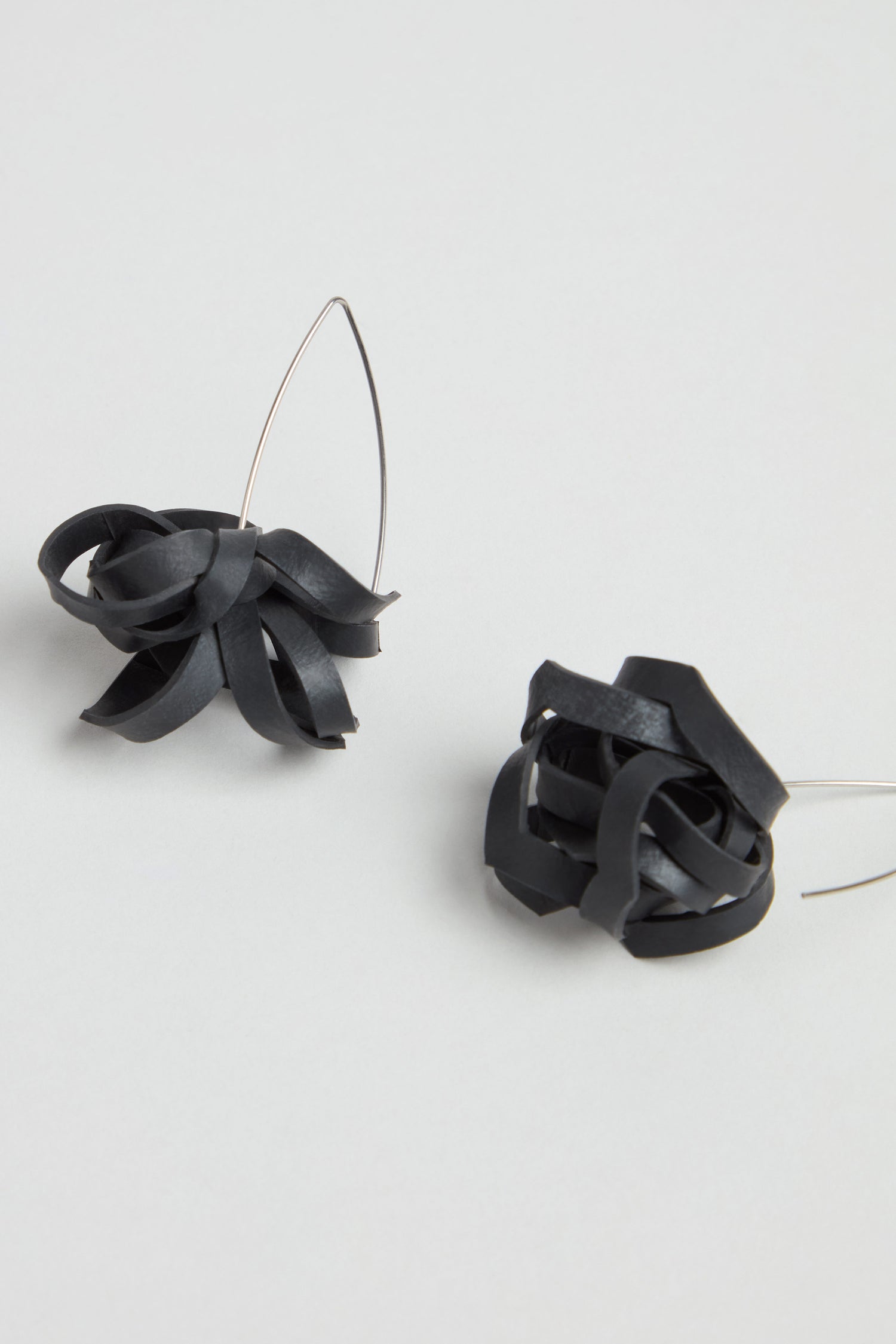 A pair of Black Pom Pom Earrings featuring sculptural, upcycled designs with twisted, ribbon-like forms and thin metal hooks, shown against a light gray background.