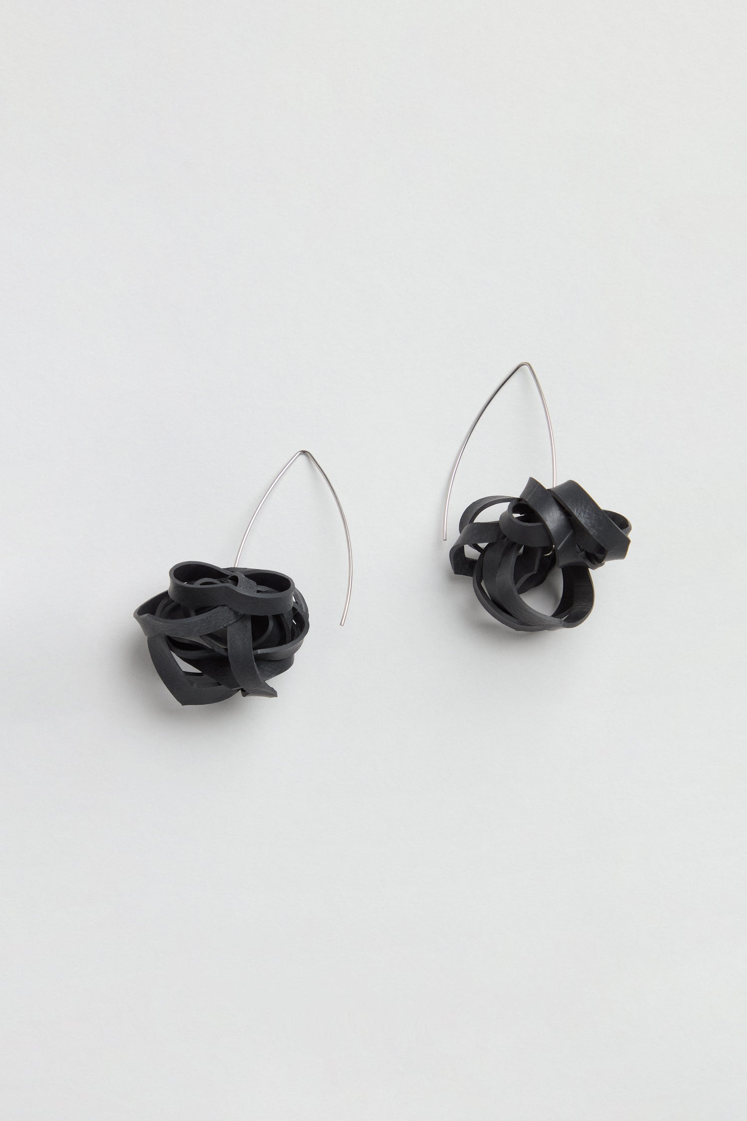 A pair of Black Pom Pom Earrings made from upcycled bicycle inner tubes, featuring black tangled loops and thin, curved silver hooks, displayed on a plain light background.