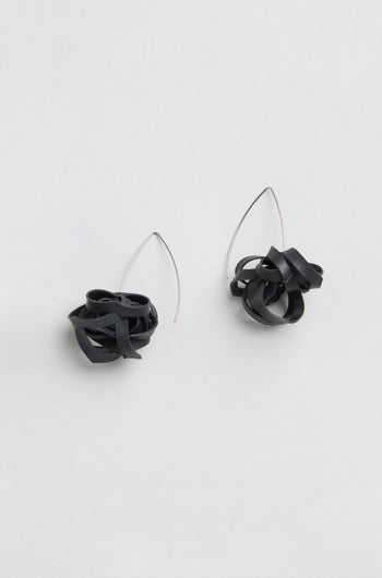 A pair of Black Pom Pom Earrings made from upcycled bicycle inner tubes, featuring black tangled loops and thin, curved silver hooks, displayed on a plain light background.