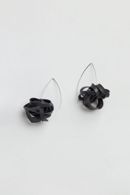 A pair of Black Pom Pom Earrings made from upcycled bicycle inner tubes, featuring black tangled loops and thin, curved silver hooks, displayed on a plain light background.