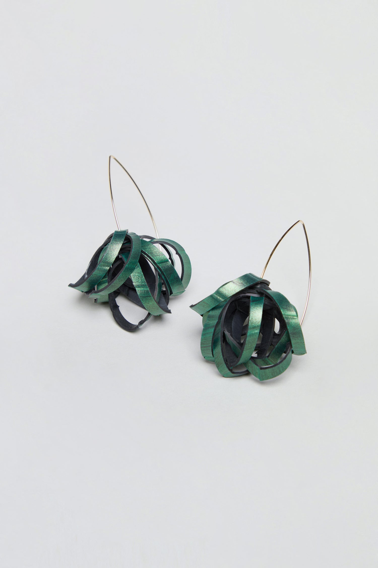 Introducing the Metallic Green Pom Pom Earrings: These upcycled earrings showcase green and black ribbon-like loops, skillfully crafted from reclaimed bicycle inner tubes into a spherical pom-pom shape. The drop-style design features thin, curved metal hooks, and is elegantly presented against a simple light backdrop.