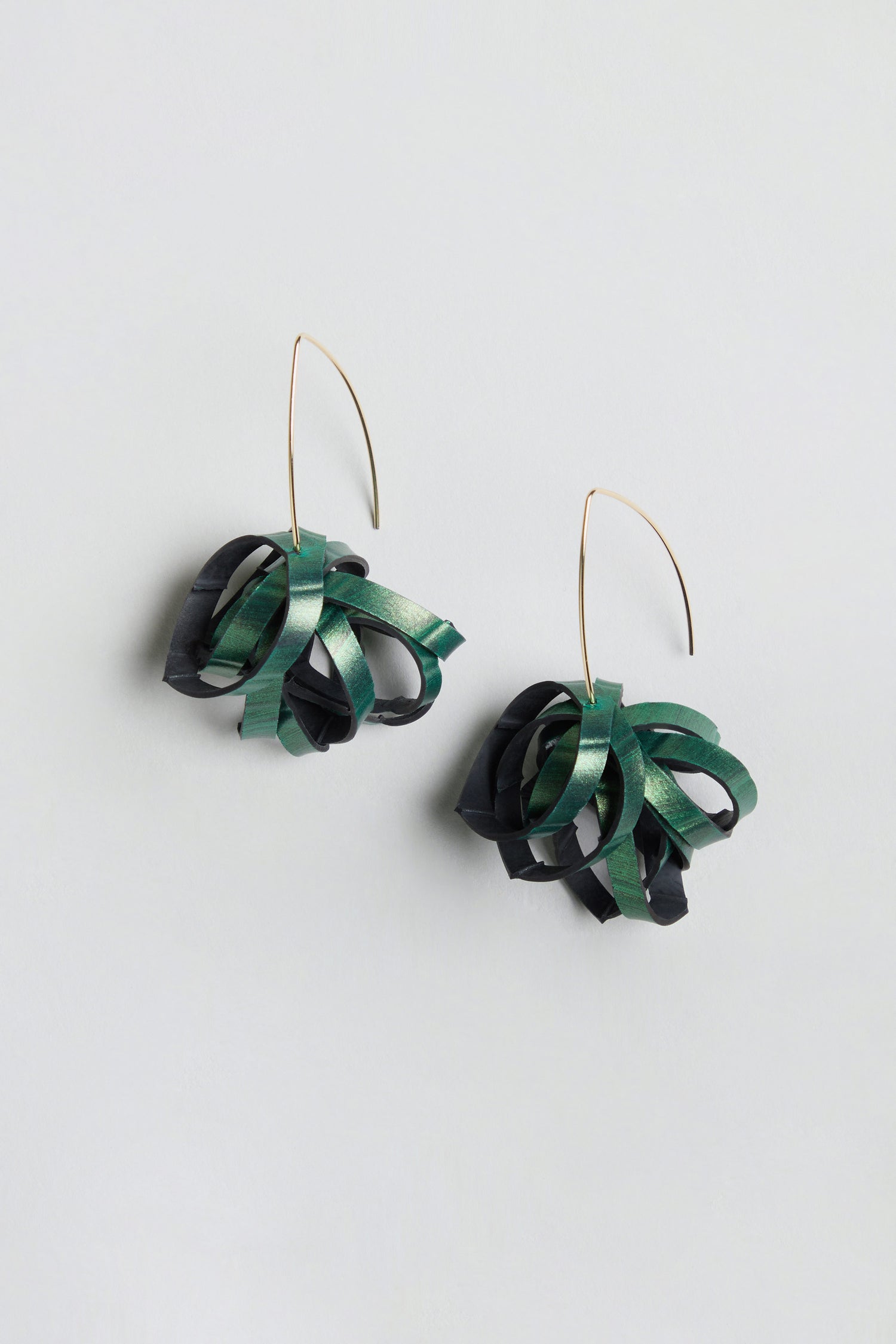 Metallic Green Pom Pom Earrings featuring gold curved hooks and looped, ribbon-like green and black accents crafted from reclaimed bicycle inner tube, displayed on a light grey background.
