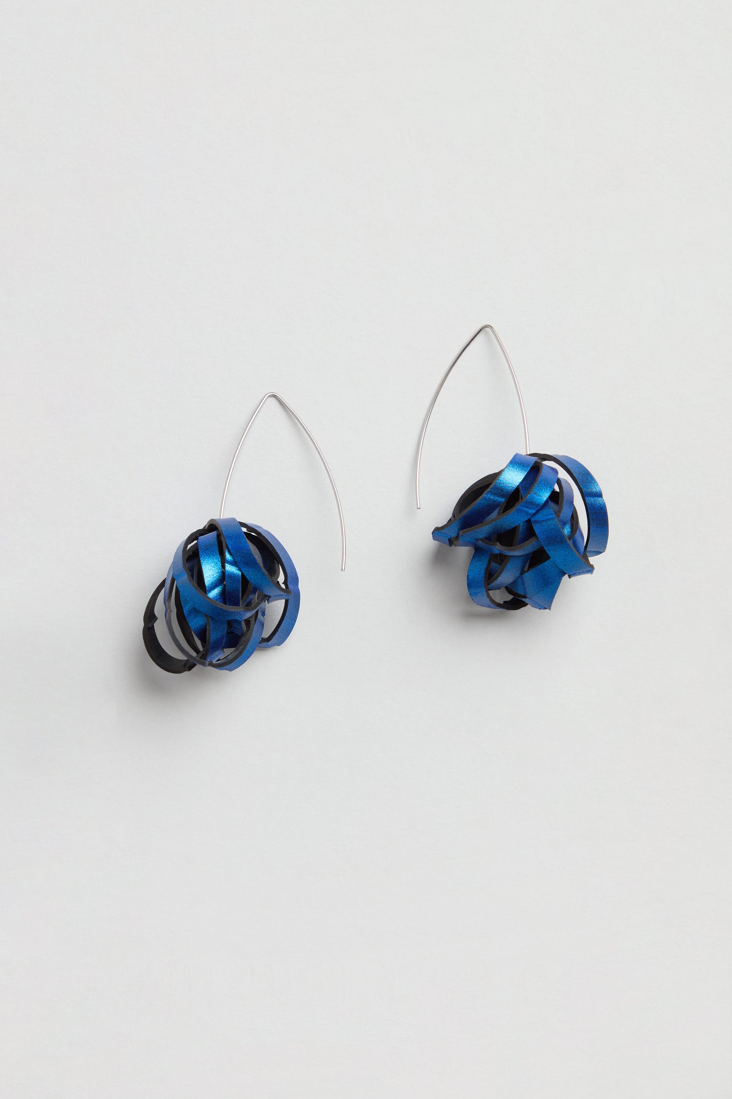 Metallic Blue Pom Pom Earrings: Upcycled from bicycle inner tubes, these earrings feature silver hooks and metallic blue with black ribbon-like loops, artfully shaped into abstract spheres.