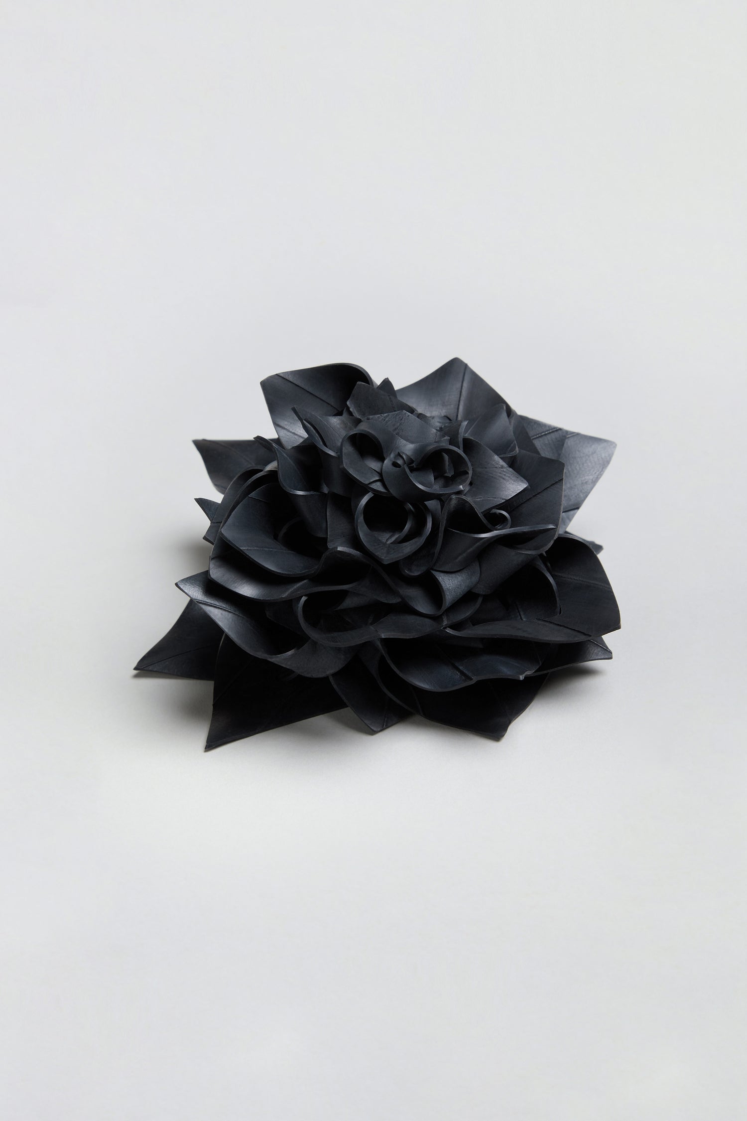 A Rose Corsage, crafted from a black bicycle inner tube and featuring multi-layered pointed petals, is displayed against a plain light gray background.