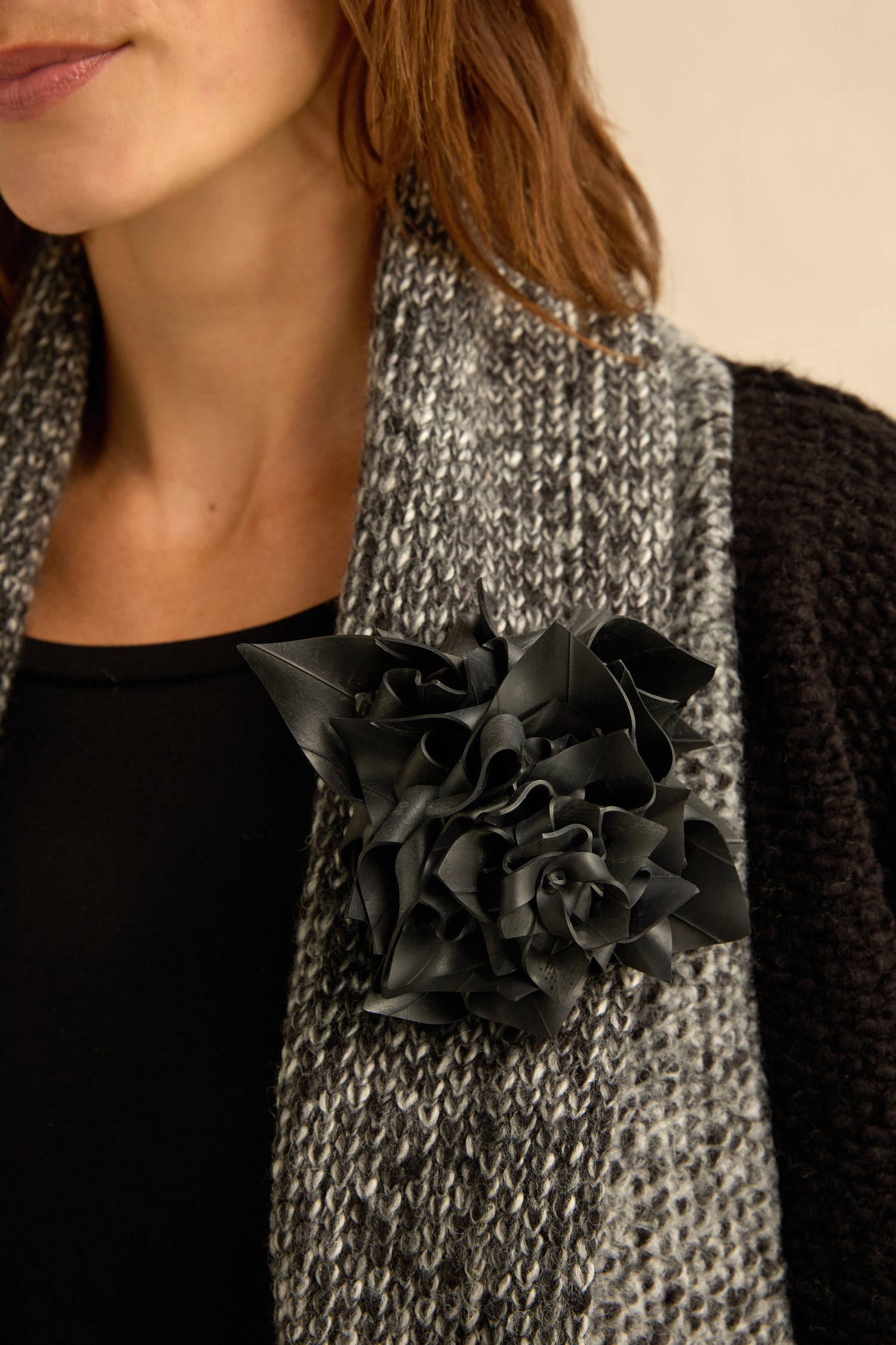 A woman wearing a black top and a grey knit scarf, adorned with the Rose Corsage—a large upcycled rose crafted from bicycle inner tube.