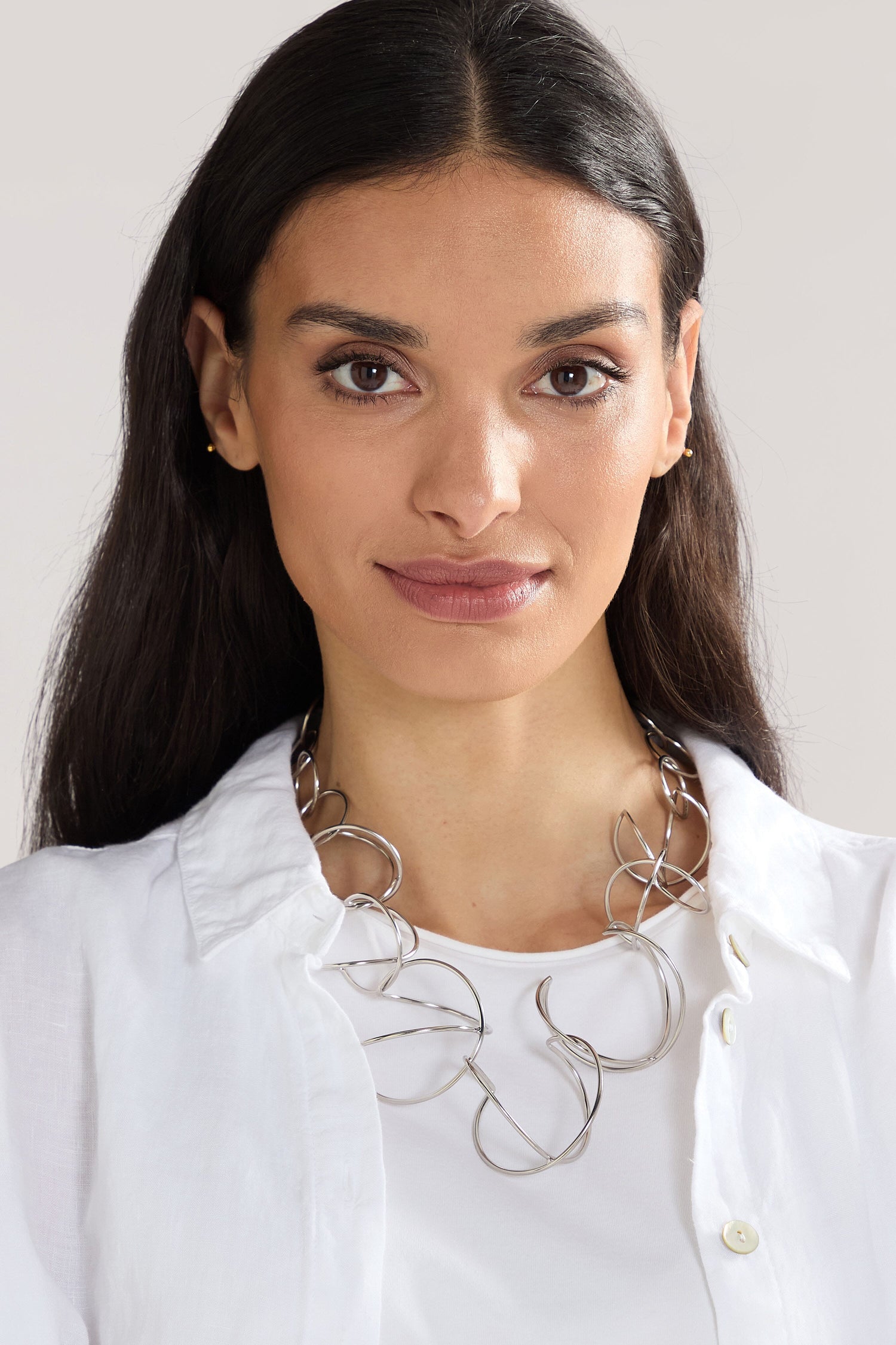 A person with long dark hair wearing a white shirt and a large, contemporary Handmade Links Necklace made of 24k gold plated brass, looking directly at the camera.