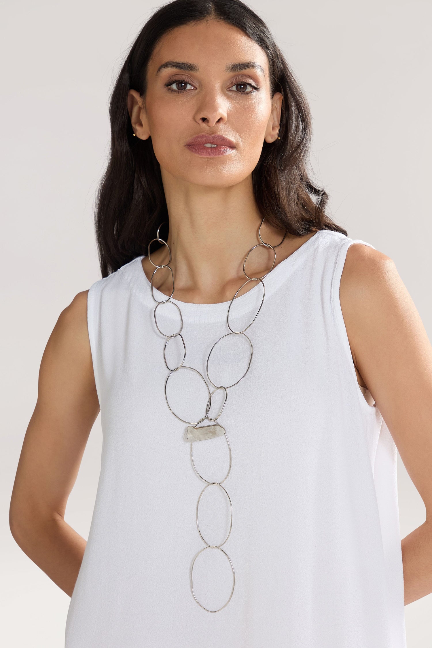 A woman in a sleeveless white top wears the Handmade Crystal Quartz Rings Necklace, featuring long, oval-linked silver chains adorned with semi-precious stones, standing against a neutral background.