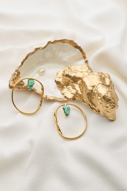 Two Handmade Agate Hoop Earrings, adorned with semi-precious agate stones, displayed next to an open golden oyster shell containing a single pearl, all placed on a white textured fabric background, exemplify the elegance of handmade jewelry.