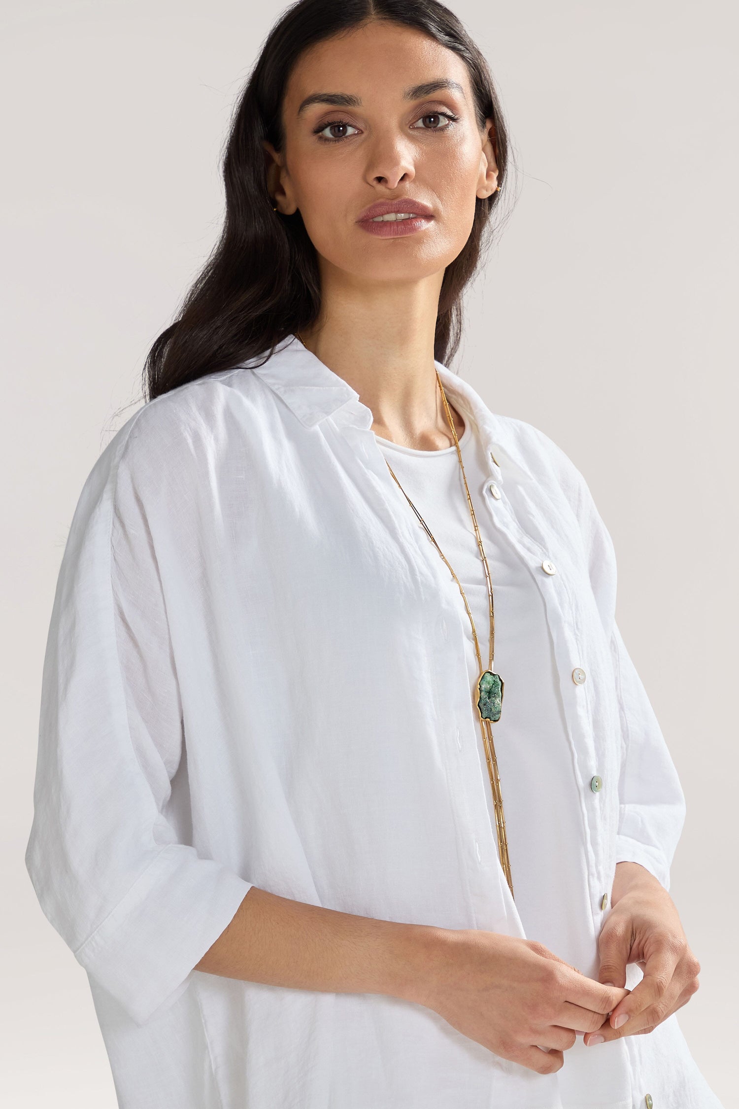 A woman with long dark hair wearing a white button-up shirt and a Handmade Gold Plated Agate Pendant, standing against a plain background.