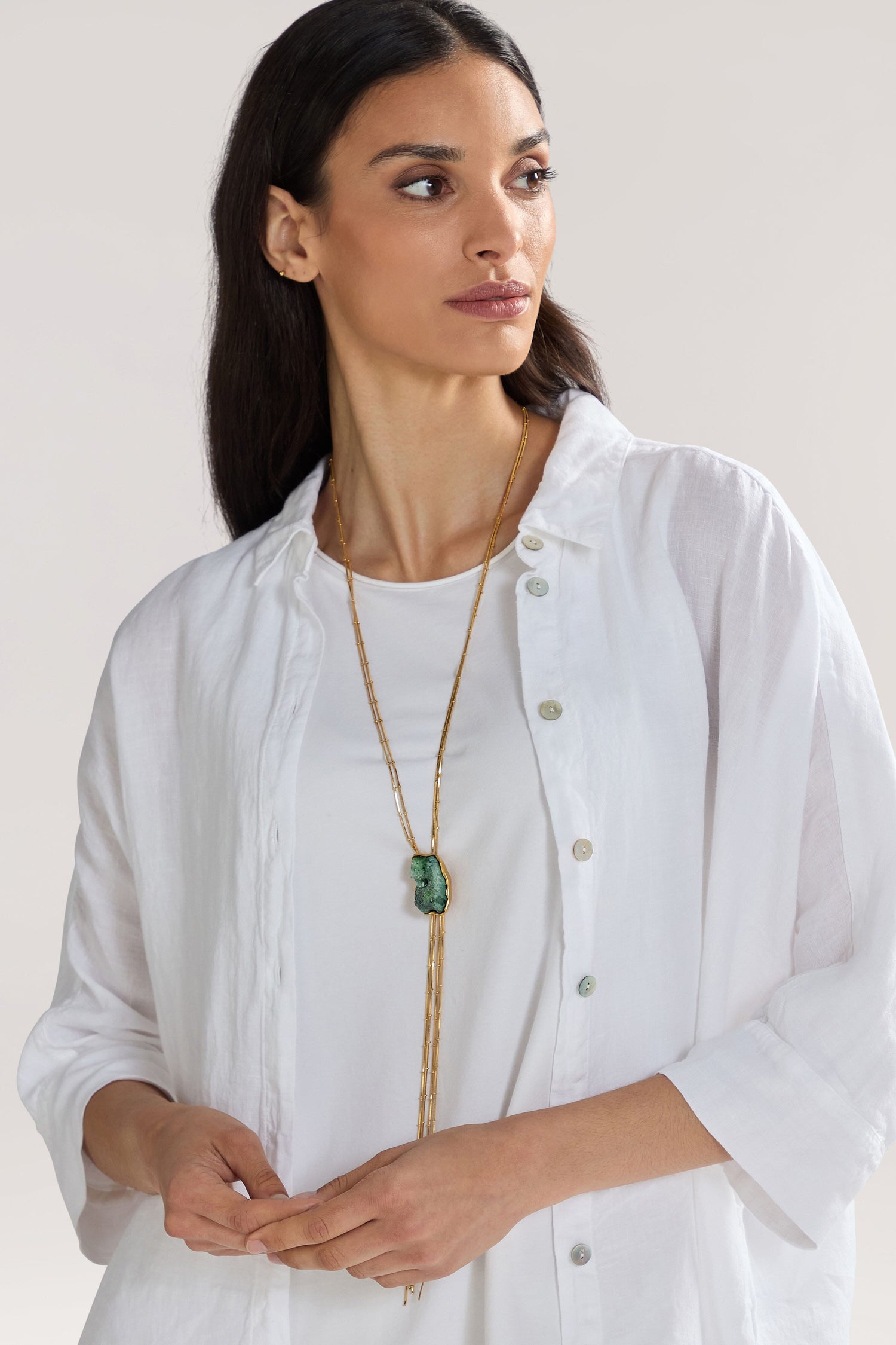 A woman with long dark hair, wearing a white shirt and a Handmade Gold Plated Agate Pendant necklace, poses against a light background.