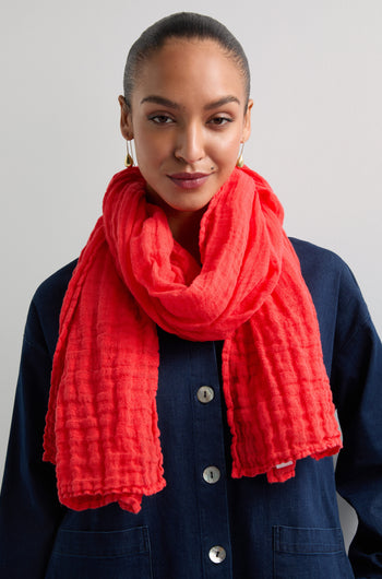 In front of a neutral background, someone sports a dark buttoned shirt and the Crinkle Linen Scarf in bright red. Their hair is neatly pulled back, highlighting the scarf as a vibrant and stylish lightweight accessory.