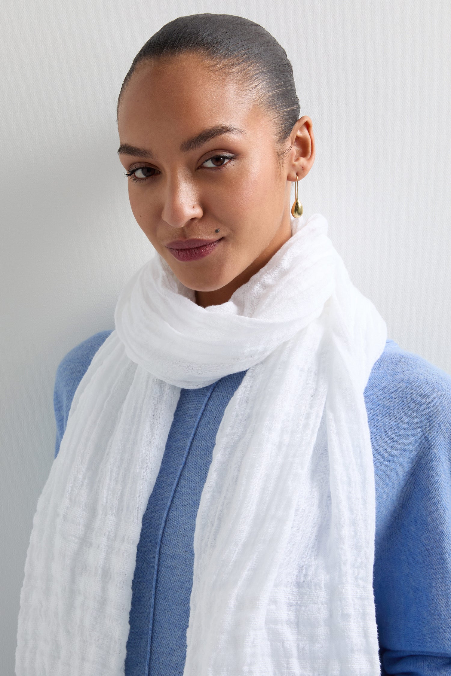 A person wears a blue top with the Crinkle Linen Scarf in white, its textured design adding depth against a simple background.