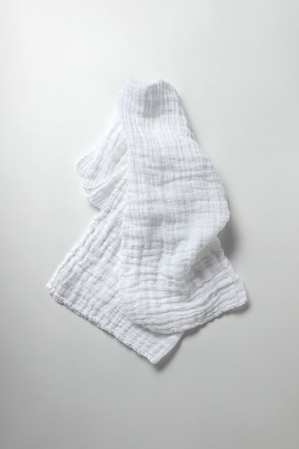 The Crinkle Linen Scarf, with its crumpled texture, rests elegantly as a lightweight accessory on a smooth, light gray surface.