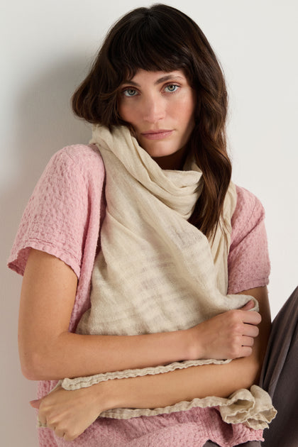 A woman with wavy brown hair wears a textured pink top and the Crinkle Linen Scarf, posing against a plain white background.