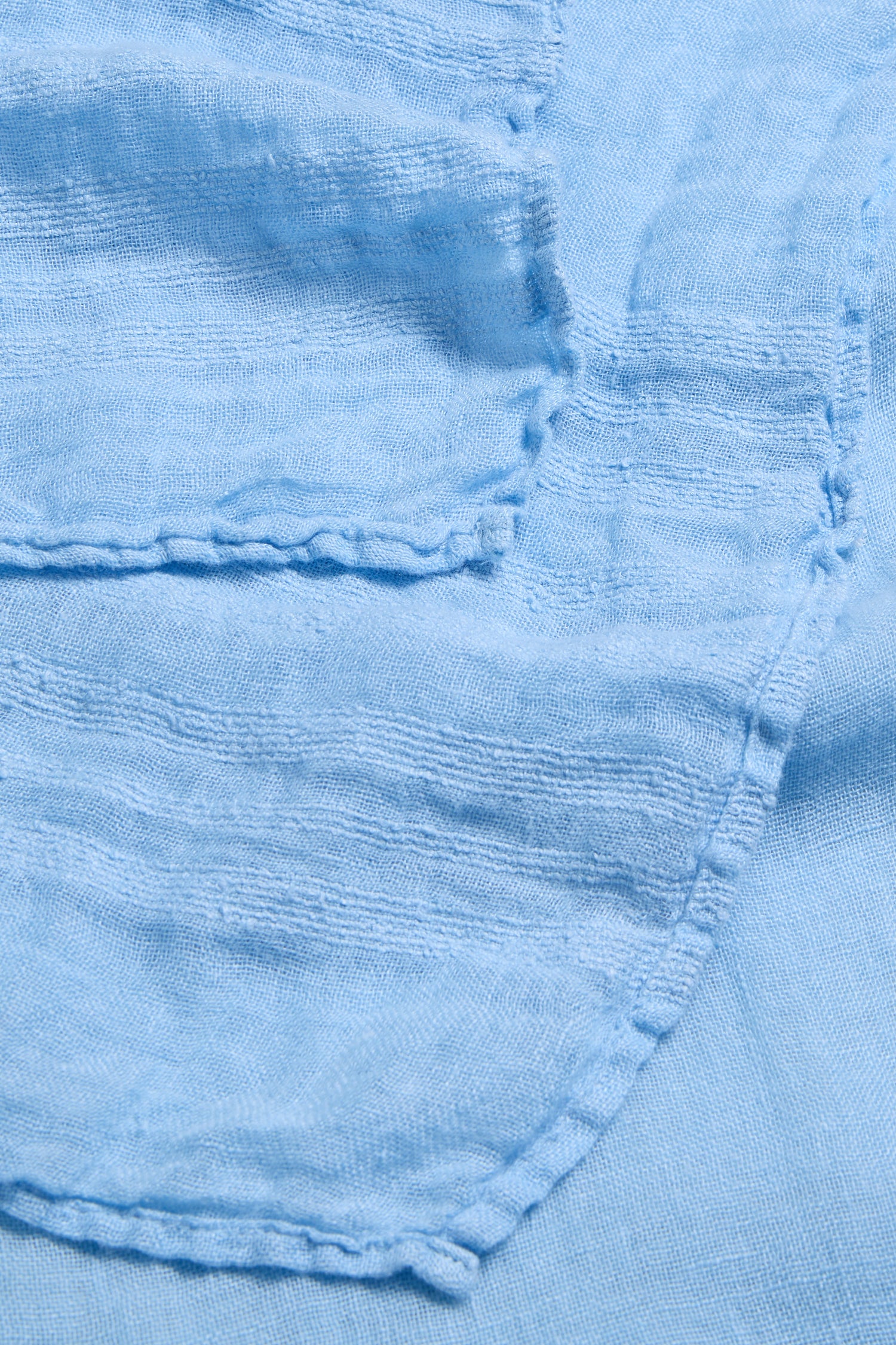 Close-up of the Crinkle Linen Scarf in light blue, showing visible stitching and layered edges that highlight its airy, lightweight texture.