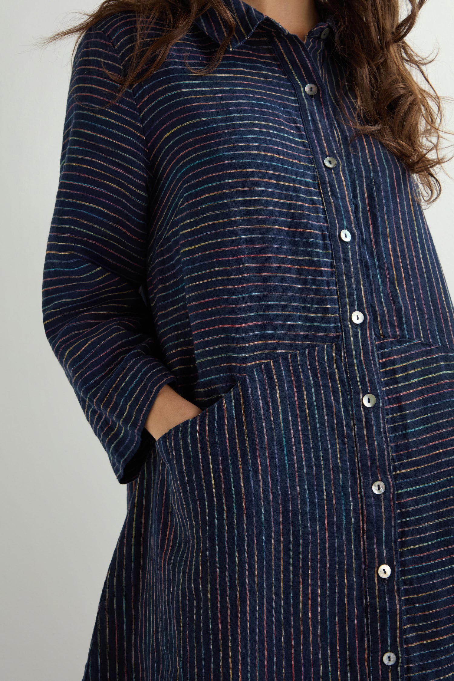 A person is wearing the Linen Navy Space Dye Stripe Shirt Dress, crafted from dyed linen, with their left hand in a pocket.