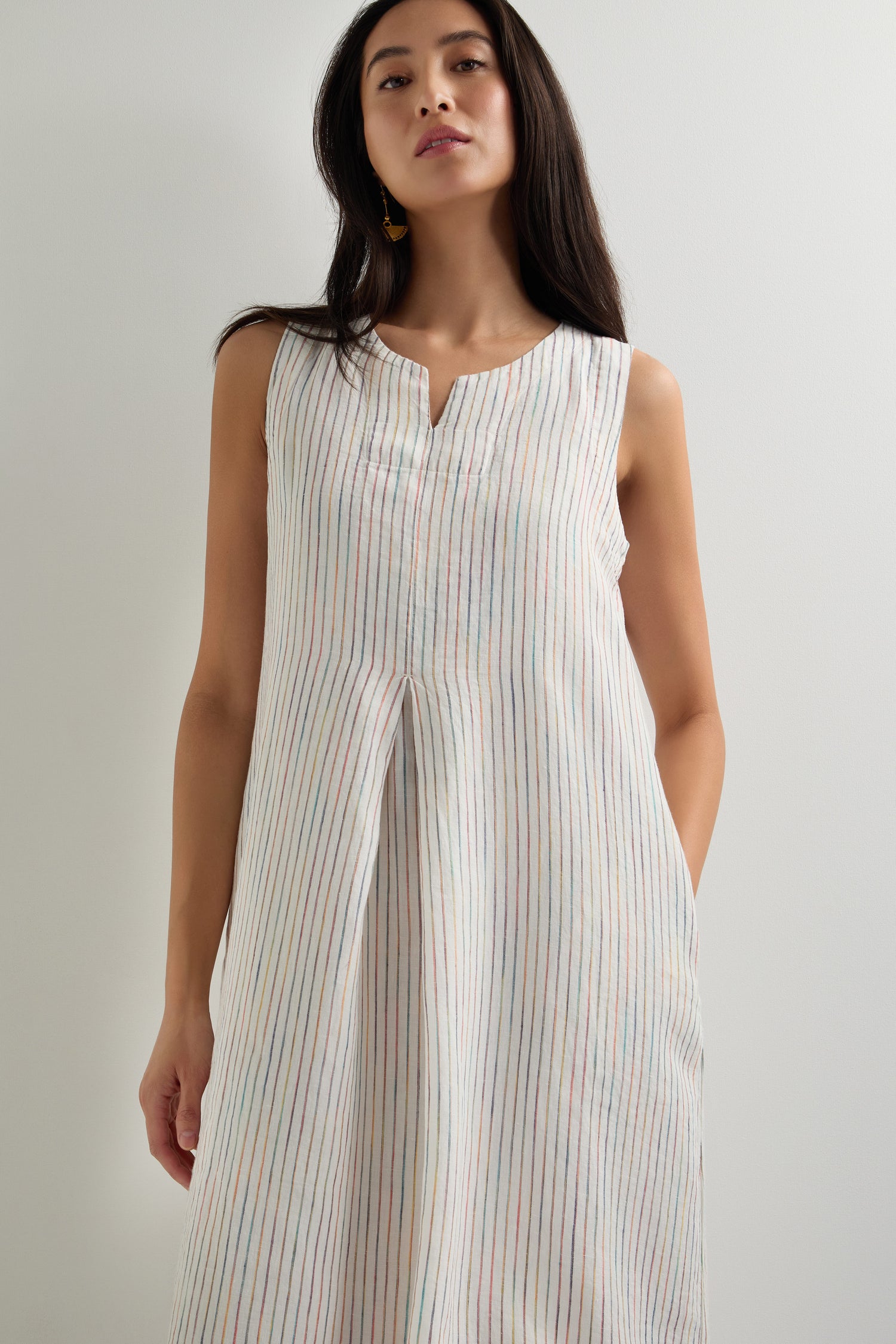 A woman models the White Space Dye Stripe Sleeveless Linen Dress, featuring vertical pastel stripes and an A-line silhouette, against a plain light-colored background.