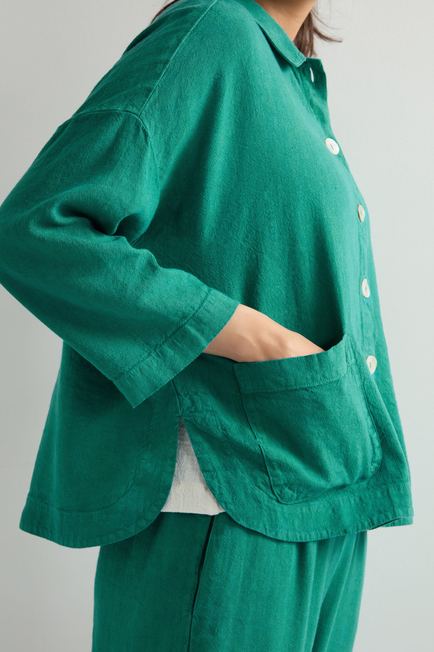 A person in a green Twisted Linen Boxy Jacket and matching pants, crafted from a breathable linen blend, stands with hands in pockets against a light background.