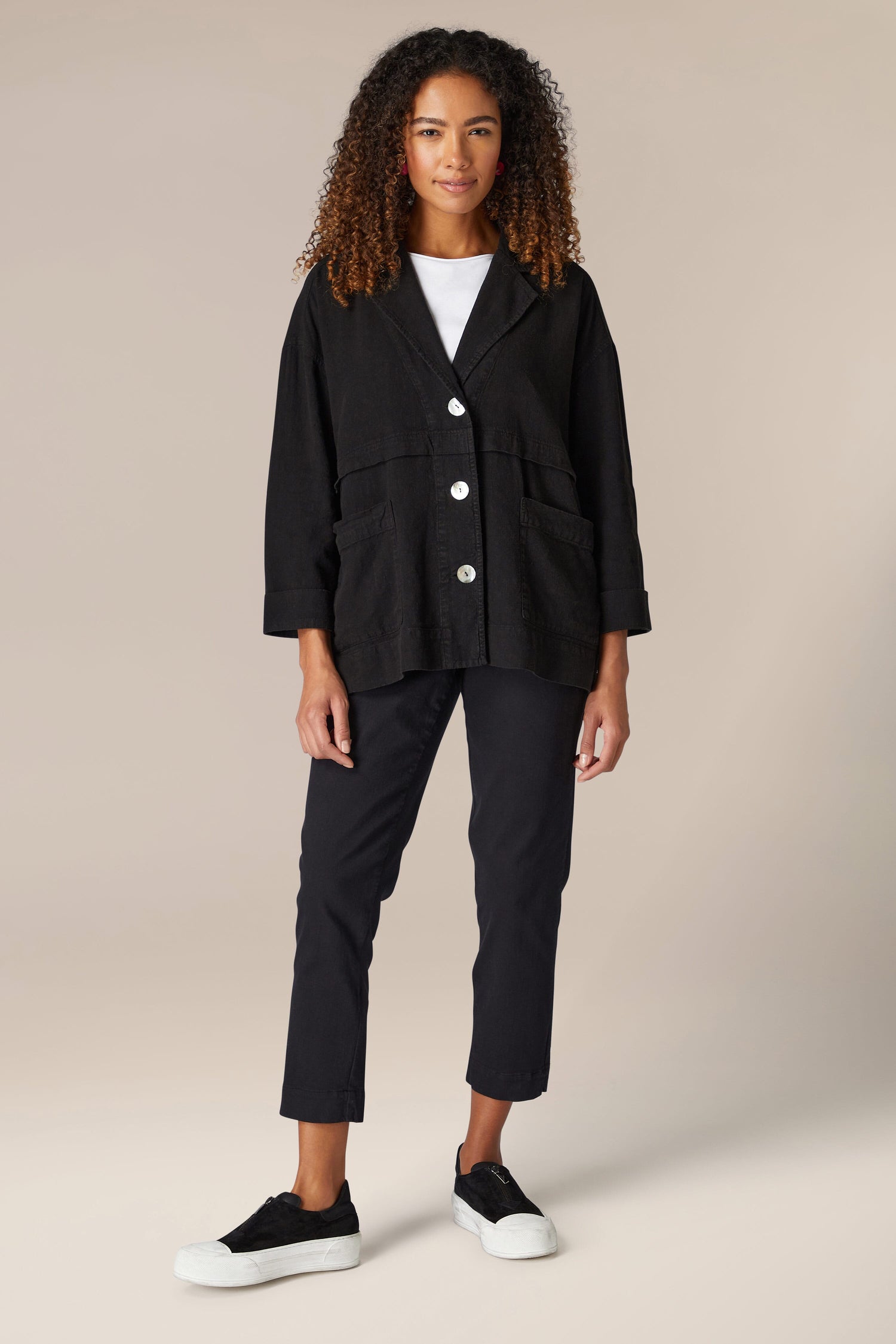 A woman wearing a Twisted Linen Boxy Jacket in black, paired with white pants.