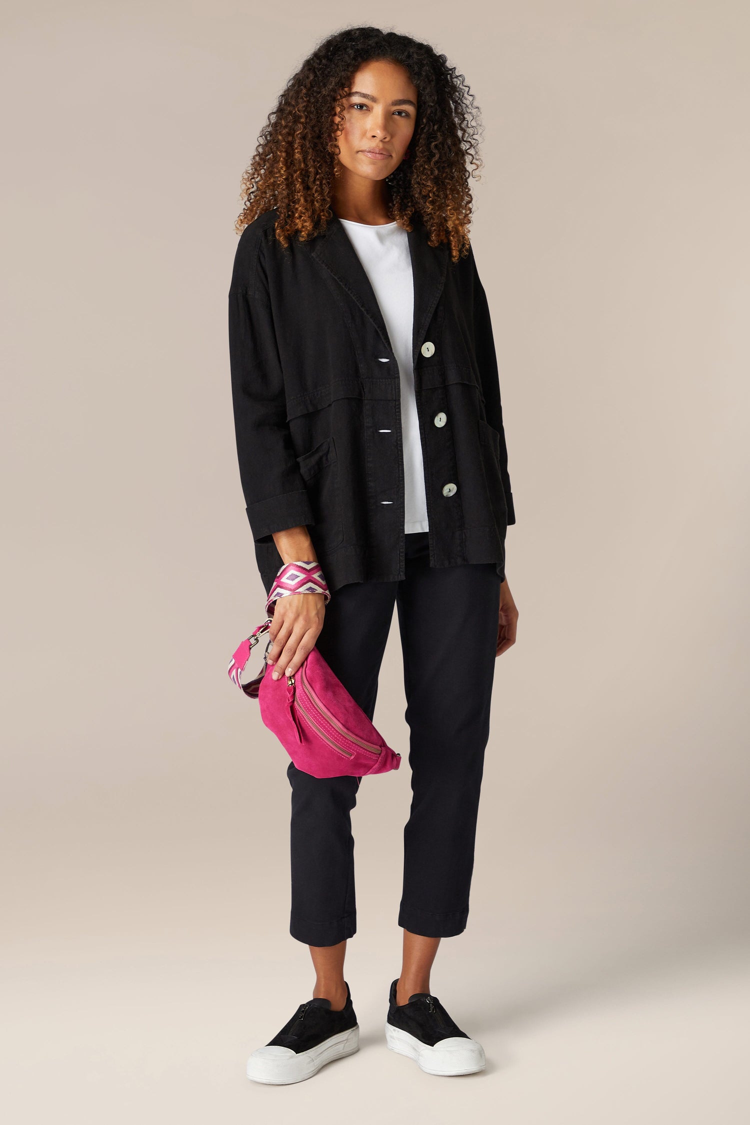 A woman wearing black pants and a pink purse is styled in the Twisted Linen Boxy Jacket, enhancing her ensemble with its boxy silhouette and premium washed twisted linen fabric.