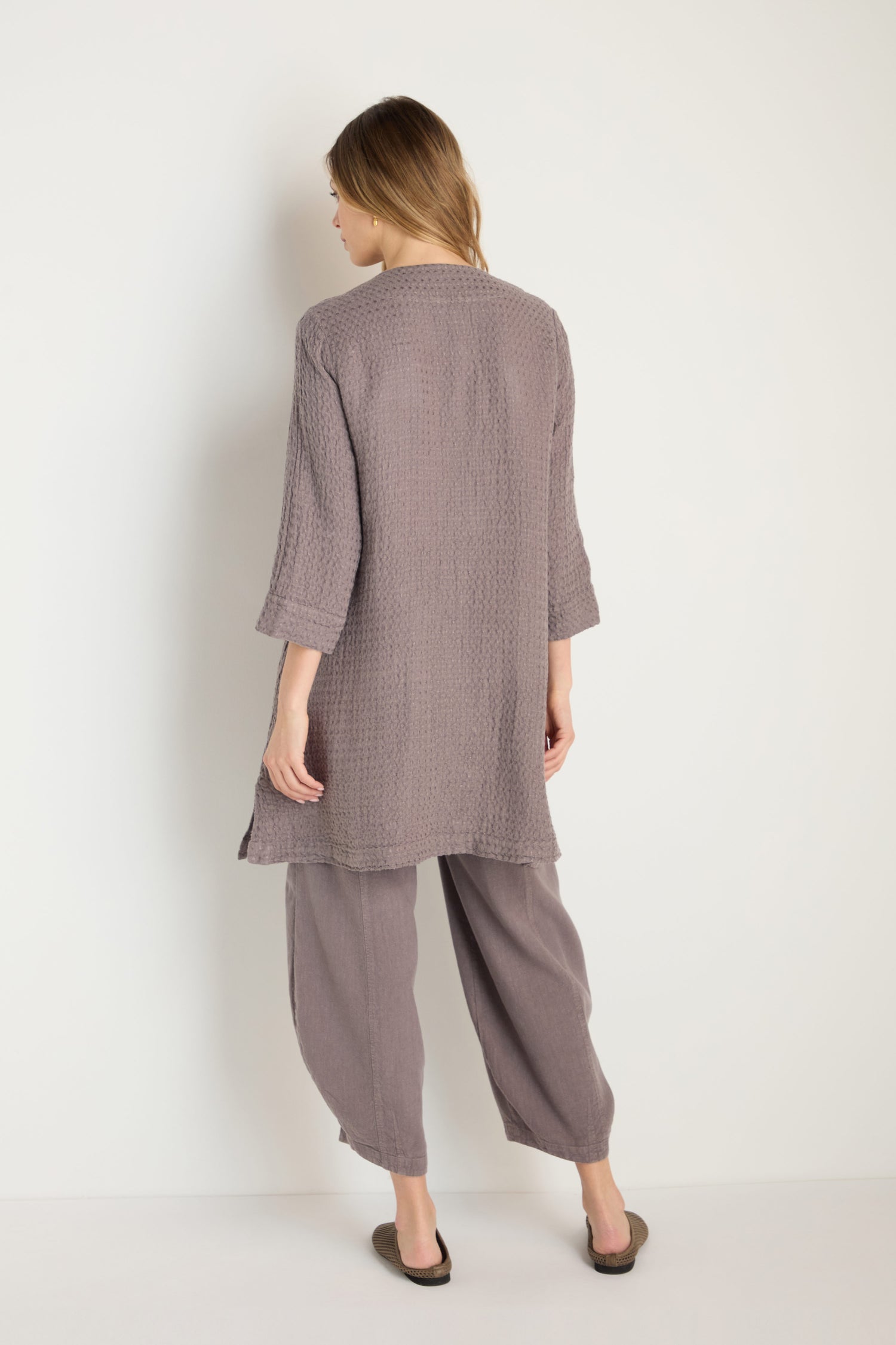 A woman faces away, wearing the Waffle Linen Long Jacket in textured mauve with matching wide-leg pants and flats, set against a plain white background.