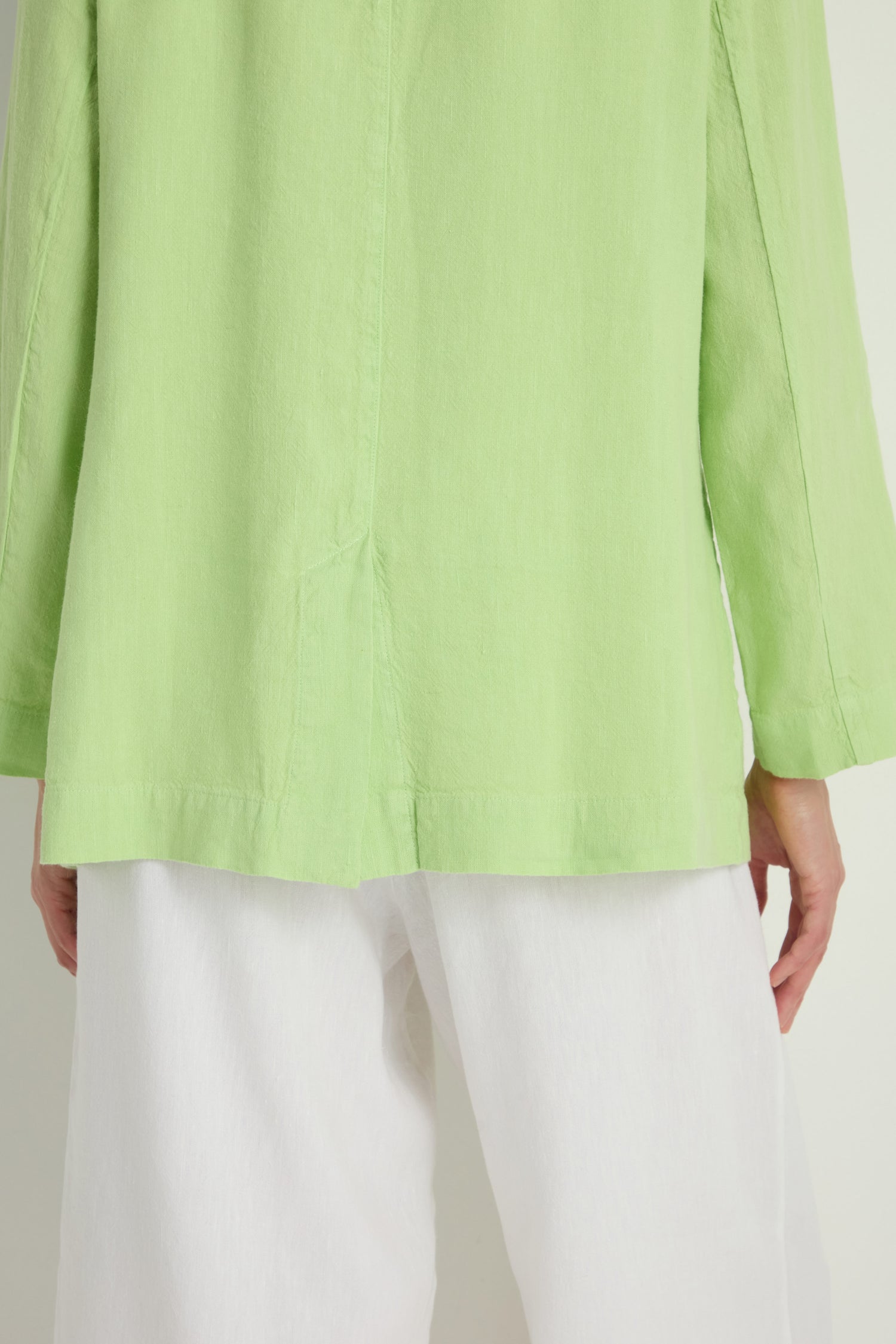 Person wearing a light green long-sleeve top and loose white pants, shown from the back with arms relaxed, styled with the Twisted Linen Relaxed Blazer for a laid-back yet refined oversized look.