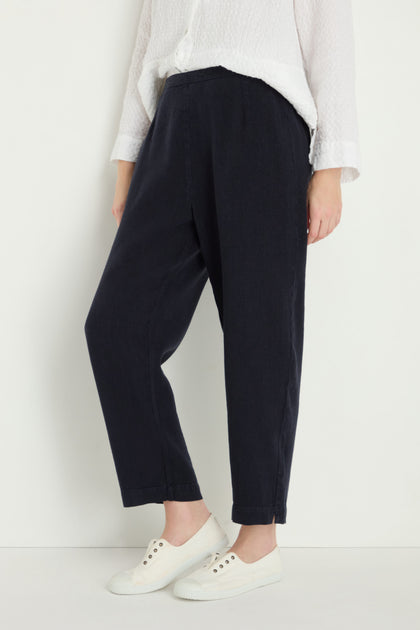 A person in black Twisted Linen Slim Trousers, a textured white long-sleeve shirt, and white sneakers stands against a plain light background.