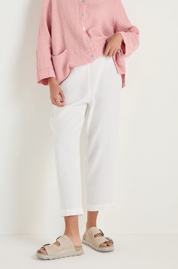 Person wearing a textured pink button-up top, beige slide sandals, and Twisted Linen Slim White Trouser, standing against a plain white background.