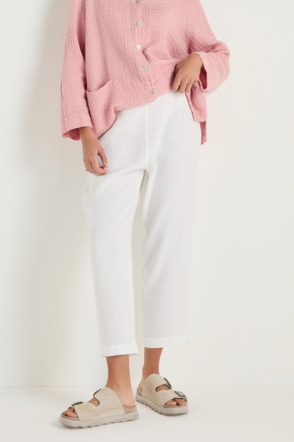 Person wearing a textured pink button-up top, beige slide sandals, and Twisted Linen Slim White Trouser, standing against a plain white background.