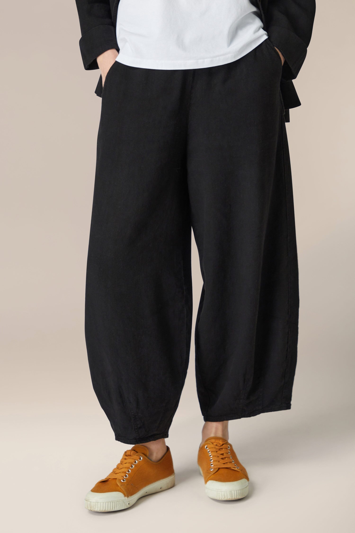 A woman wearing black Twisted Linen Bubble Trousers made of linen fabric with an elasticated waistband, paired with a white t-shirt.