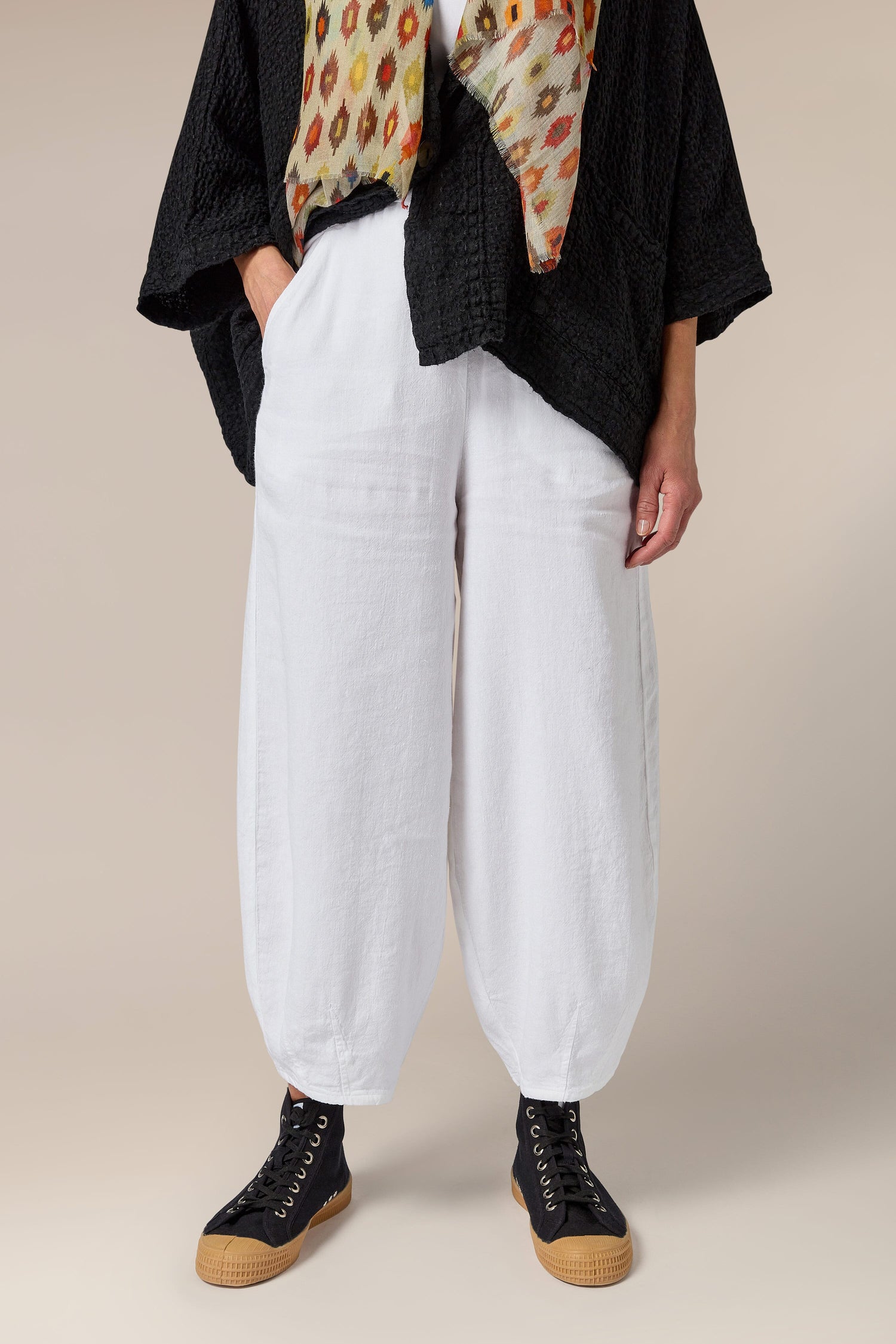 A woman wearing white Twisted Linen Bubble Trouser made of linen fabric and an elasticated waistband, paired with a black scarf.