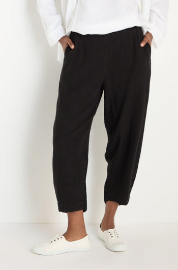 A person wears the Twisted Linen Crop Bubble Trouser in black, styled with a white top and white sneakers, standing against a plain white background with hands in pockets.