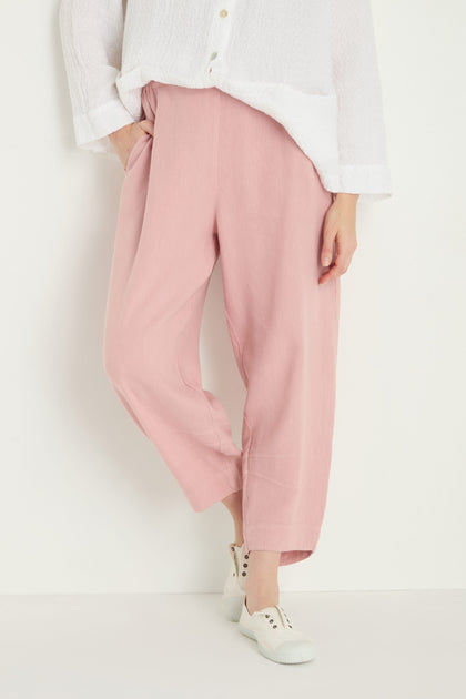 Wearing Twisted Linen Crop Bubble Trouser in light pink with a relaxed bubble silhouette, paired with a textured white long-sleeve shirt and white sneakers; breathable linen adds comfort and effortless style against a plain white background.