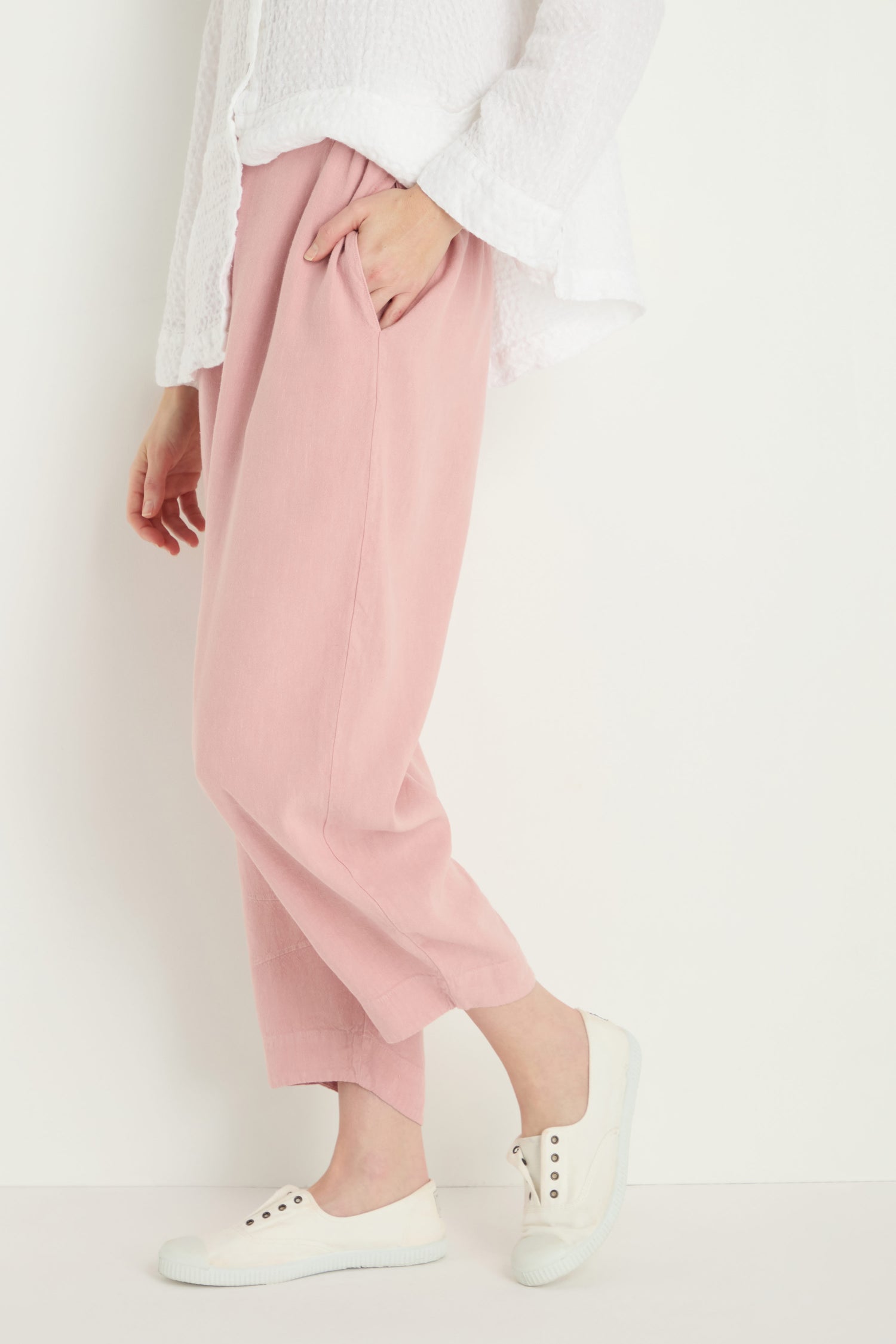 Wearing a white textured top, Twisted Linen Crop Bubble Trouser in pink, and white sneakers, standing against a plain light background.