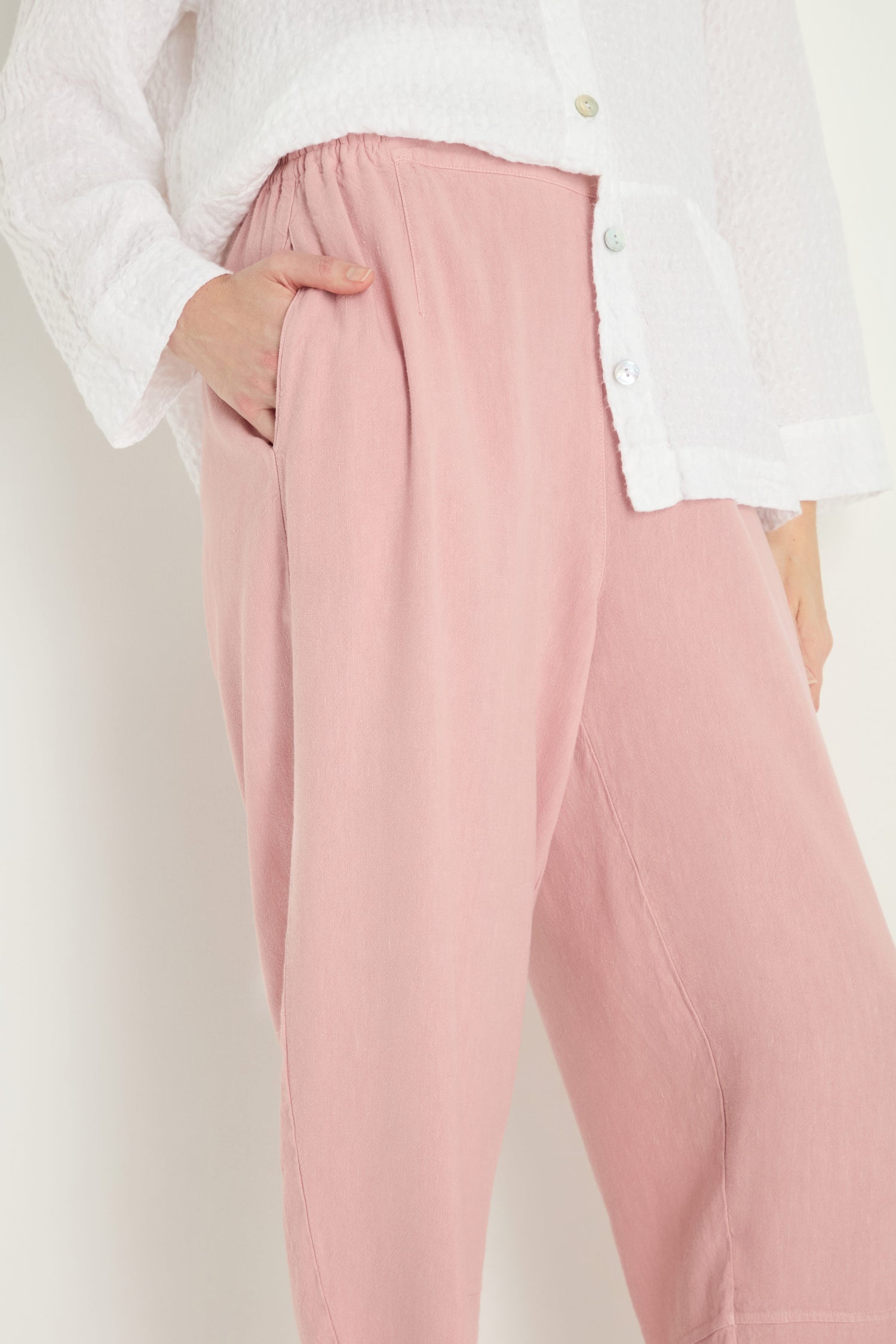 Person wearing a white textured button-up top and Twisted Linen Crop Bubble Trouser in pink, featuring a loose bubble silhouette, one hand in the pocket; shown from shoulders to ankles.